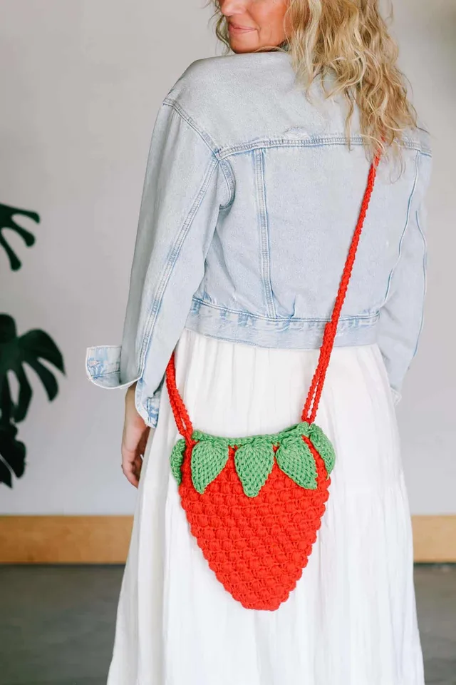 Crochet strawberry purse pattern featuring a red textured strawberry-shaped bag, green crochet leaves, and a shoulder strap.